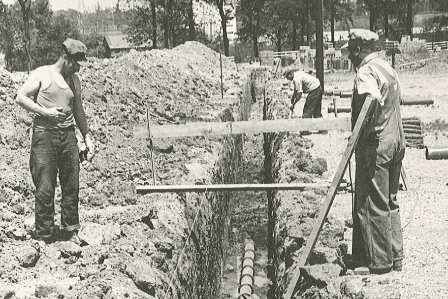 Black and white image of men building a trench with lumber stretching across a dugout section