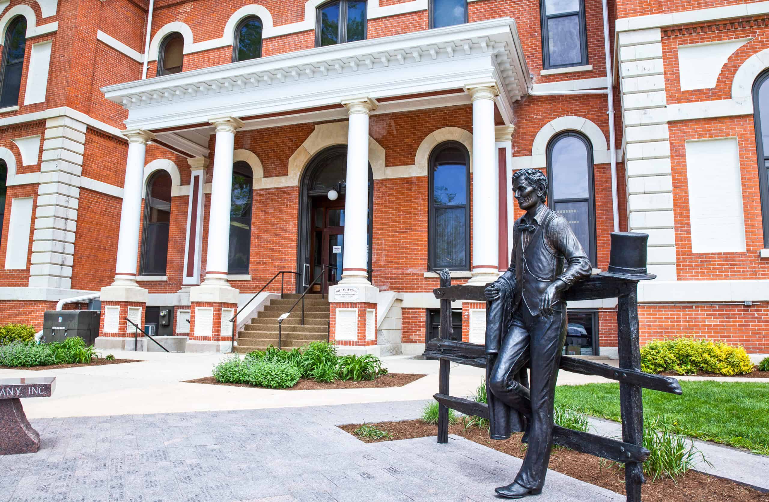 Close up image of the front of an older styled brick building with an iron statue of a man leaning against a fence