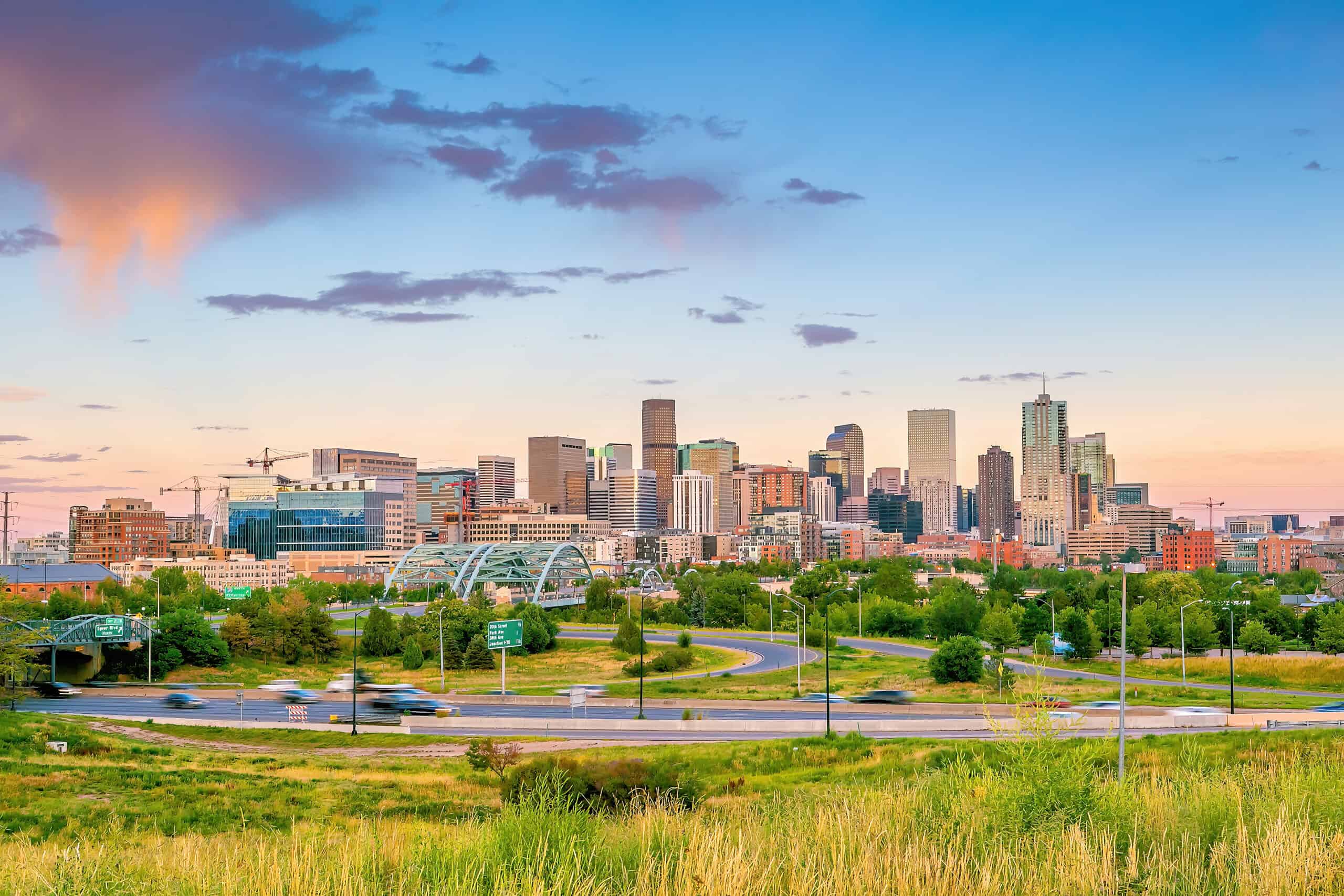 Skyline view of Denver with a view of a grassy area with skyscrapers lining the background during sunrise or dusk